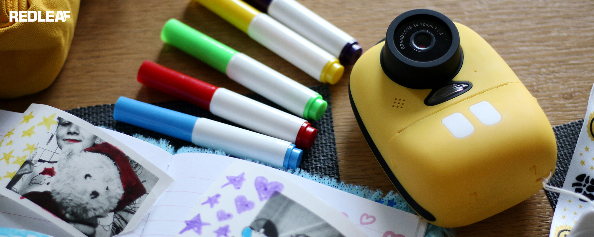 Aparat fotograficzny z drukarką dla dzieci Redleaf BOB leżący na biurku razem z kolorowymi mazakami